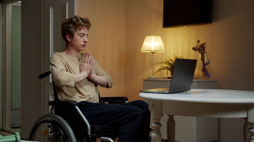 Young man meditating while sitting by laptop at home