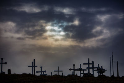 View of cross at cemetery against cloudy sky