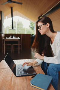 Young woman using mobile phone while sitting on table