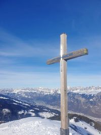 Cross on snowcapped mountain against blue sky