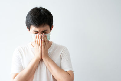 Portrait of young man covering face against white background