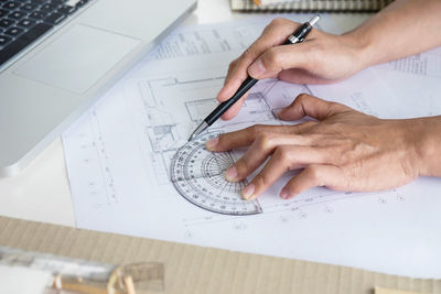 Cropped hands of architect drawing blueprint in office