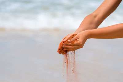 Cropped image of hands holding sand at beach