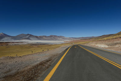 Road leading towards mountains against clear sky