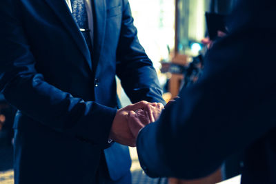 Midsection of gay couple holding hands during wedding ceremony