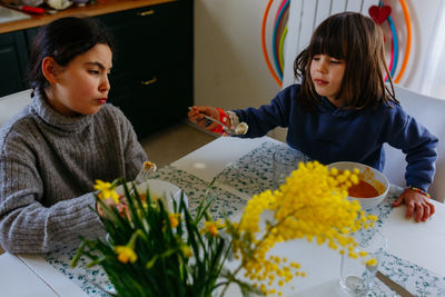 Two sisters eating lunch at home at white table with yellow flowers