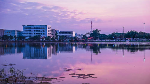 Reflection of buildings in lake against sky at sunset