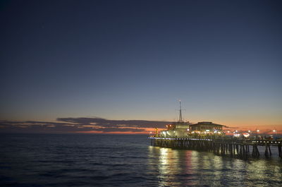 Illuminated santa monica pier over sea against sky during sunset