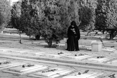 Rear view of woman sitting on cross against trees