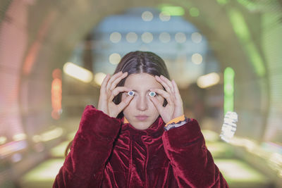 Woman holding artificial eyes while standing against illuminated lights