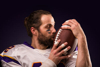 Portrait of young man holding ball against black background