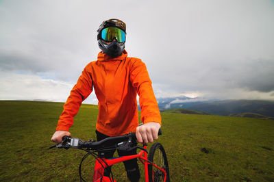 Portrait of a male downhill cyclist in a full face helmet and goggles with an orange windbreaker