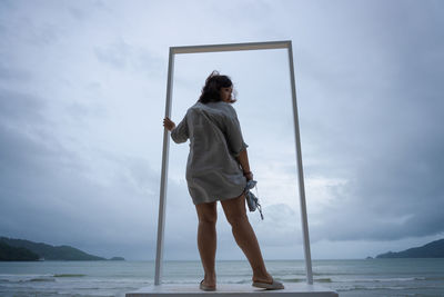 Full length of woman standing at sea shore against sky