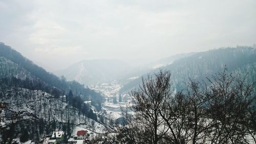 Trees against mountains and sky during snowfall