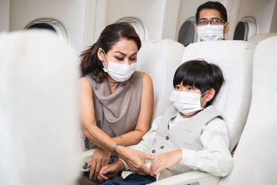 Woman and son sitting in airplane wearing face mask