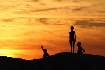 Silhouette people standing on rock against sky during sunset