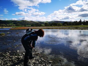 Side view of woman standing by lake against sky