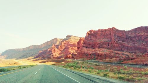 Road by rocky mountains against clear sky