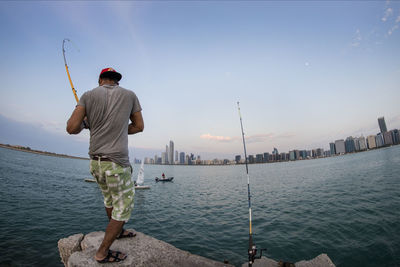 Rear view of man fishing in sea against sky