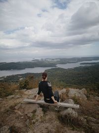 Man sitting on rock against sky