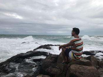 Boy standing on rock at beach against sky