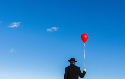 Rear view of man holding balloon against blue sky