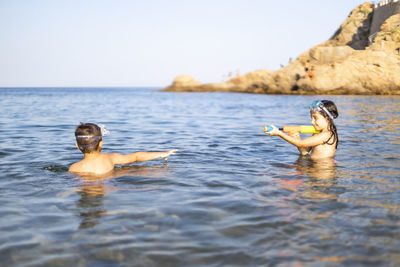 Siblings playing in sea against sky