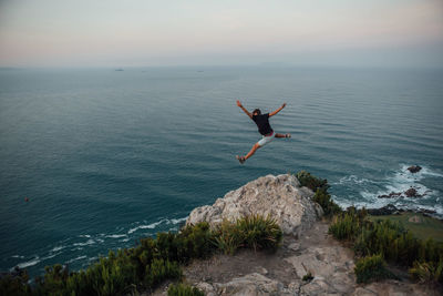 Full length of man jumping against sea and sky during sunset