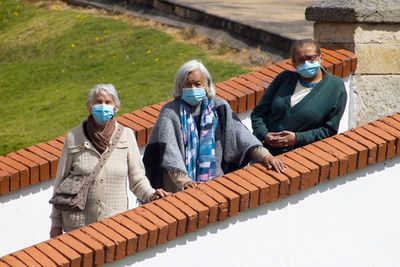 Senior people wearing mask standing by brick wall outdoors