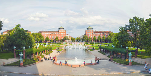 People at fountain in city against sky