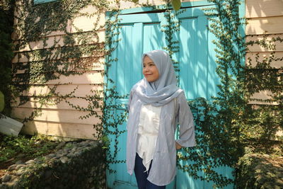 Smiling young woman standing against plants and colorfull door