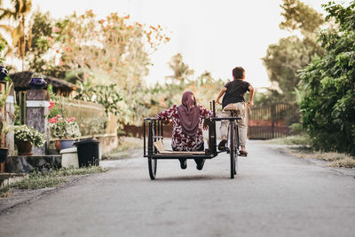 Rear view of boy with mother riding pedicab on road