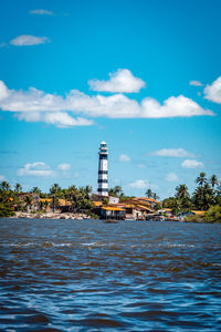 Lighthouse amidst sea and buildings against sky