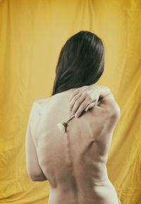 Woman in yellow satin dress showing her back in a romantic attitude with a daisy