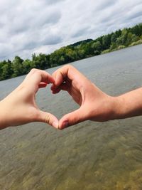 Cropped hands making heart shape against sky