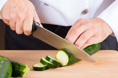 Midsection of chef cutting zucchini in commercial kitchen