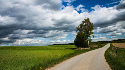 Empty road amidst field against sky