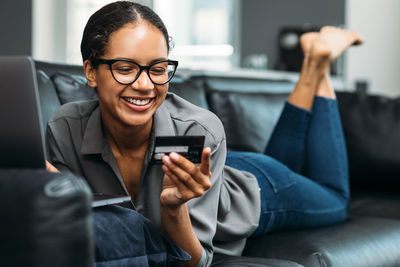 Smiling woman holding credit card while using laptop