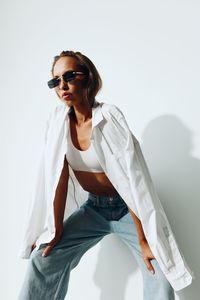 Young woman wearing sunglasses while standing against white background