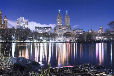 Reflection of illuminated modern buildings in lake at night during snowfall