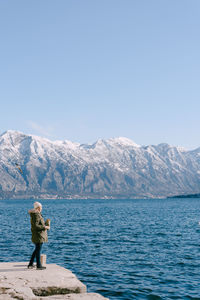Rear view of person standing on snowcapped mountains against clear sky