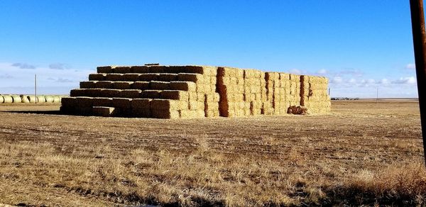 Hay bales on field against clear blue sky