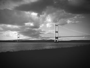 Suspension bridge over river against cloudy sky