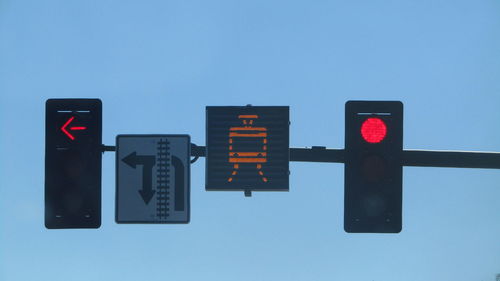 Low angle view of illuminated stoplights with road sign against clear sky