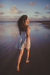 Woman standing at beach against sky during sunset