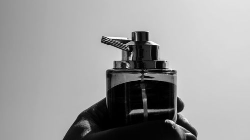 Cropped hand holding bottle against clear sky on sunny day