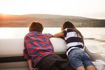 Rear view of siblings in boat on lake against mountains