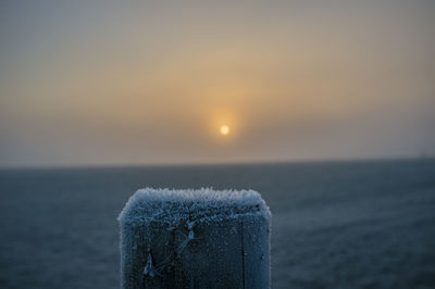 Close-up of wooden posts on sea against sky during sunset