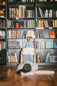 Girl reading book while lying down with feet up on shelf in bookstore