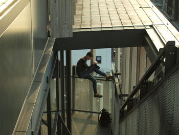 High angle view of mid adult woman photographing while sitting on railing